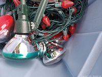 Close-up image of green corded string lights with red cone-shaped bulbs and attached reflective silver flood light units.