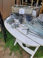 Overview of white metal wire pegboard baskets and multiple metal pegboard hooks scattered on a white table outdoors.