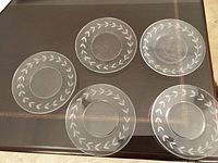 Top-down view of the set of five clear glass dessert or salad plates arranged on table, showing the leaf border design on the underside of each.
