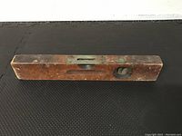 Wooden level angled showing side with horizontal vial and round vertical vial, wood shows signs of wear and age.