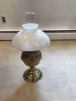 Full view of the vintage brass kerosene table lamp with milk glass dome and glass chimney on carpeted floor.