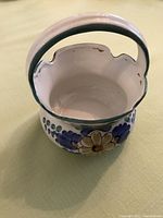 Front view of white ceramic basket showing scalloped rim, handle, and floral decorations.