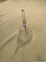 Glass crystal dinner bell shown standing on a yellowish fabric surface, displaying its clear body and etched floral pattern.