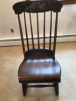 Front view of the dark brown primitive Boston style rocker chair showing its contoured wooden seat and 7 vertical back spindles.