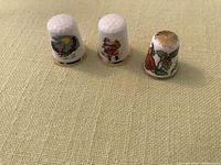 Front view of three Christmas-themed fine bone china thimbles on beige fabric background showing Santa and festive imagery.