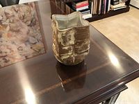 View of ceramic vase on a dark wooden table showing its brown and white textured surface and unique squared shape.