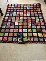 Full view of the colorful granny square afghan laid flat on the floor showing the entire blanket with black borders and multicolored squares.