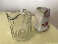 Two pitchers displayed side by side: square ceramic pitcher with floral pink rose design, adjacent to clear glass pitcher with rounded handle and spout