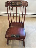 Front view of red painted Boston rocking chair showing seven spindle back with floral and cornucopia hand painted top rail, plank scroll seat with painted floral accent, and turned legs.
