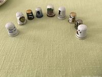Row of nine souvenir thimbles from various locations, showing decorative details on front and side faces