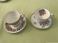 Top view of two matching sets of fine bone china teacups and saucers with floral designs and gold trim sitting on a green cloth background.