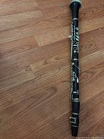 Full view of a fully assembled wooden clarinet with silver keys lying on wooden floor.