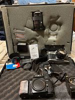 Minolta 9000 AF Maxxum camera body with visible damage and tape on grip, along with another manual camera, lenses and accessories arranged in a foam case.