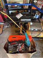 Photo showing the DeWalt air compressor, Ridgid reciprocating saw case, Bosch motor box, blue electric drill, manual puller, sanding discs, and other tools in a cardboard box and surrounding area.