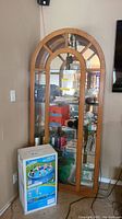 Full view of wooden curio cabinet with glass doors. Cabinet contains various items, standing next to a boxed pool.