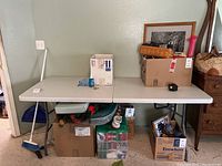 Wide view of the folding table with various items on and under it, showing the table's dimensions and general condition.