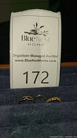Photo of five gold and gold-colored rings displayed together on a blue fabric with a Blue Nest Home auction number card behind