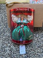 Barbie doll in green holiday dress inside clear red-trimmed oval box labeled 'Happy Holidays' and 'Special Edition'. Doll has blonde curly hair and festive dress.