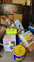 Overview photo showing stacked cardboard boxes including a boxed turkey fryer, metal candle holder, scrap wood and other household items.