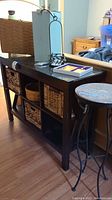 Photo showing wooden console table with glass top and three woven baskets underneath, with some decorative items on top including a box, candle holder and basket.