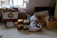Photo of assorted boxes, plastic bags containing toys, puzzles, craft supplies, and household items piled near a window.