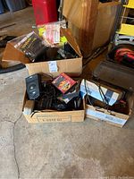 Three cardboard boxes containing gaming consoles, controllers, cables and track pieces