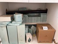 Shelving unit with multiple boxes of PartyLite products including reed diffuser refills, votives, and a large cardboard box labeled 3-wick candle.