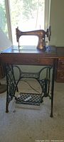 Side view of the vintage Singer treadle sewing machine mounted in wooden cabinet showing metal treadle base and machine with gold decal details.