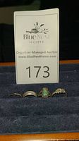 Four sterling silver rings displayed on dark velvet background with auction lot card