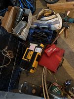 Overview photo showing tool bags, Milwaukee red cases, Kirby vacuum parts in a box, and some hand tools on a concrete floor with other items visible at edges of photo.