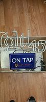 Photo showing vintage Colt 45 white neon tubing sign coiled within a cardboard box with a blue rectangular metal sign "ON TAP MALT LIQUOR BY NATIONAL".
