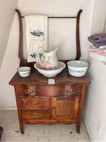Front view of vintage wooden wash stand with ceramic pitcher, bowls, and embroidered towel.