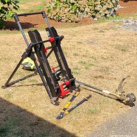 Craftsman black and red adjustable work table with clamp mechanisms and caster wheels, Ryobi weed whacker lying on ground, Fiskars loppers in front.