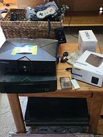 Tabletop basket with two gaming controllers, assorted cables; original Xbox console and black DVD player stacked next to basket