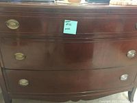 Three drawer dresser with dark polished wood, showing surface scratches. Oval brass drawer pulls visible on drawers.