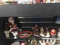 Shelf with various Christmas figurines including Santa Claus, snowmen, reindeer, and decorative bowls.
