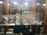 Display shelf showing multiple crystal glasses including wine glasses, cocktail glasses, and tall glasses with various etching and cuts on the crystal glassware.