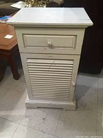 Front view of distressed shabby chic style wooden cabinet showing drawer and louvered door with round knobs.