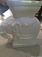 Side view of the white elephant ceramic plant holder showing detailed sculpted saddle and flat top surface.