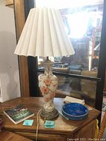Full view of vintage porcelain lamp with floral design and pleated fabric shade on wooden table
