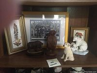 Shelf with three ceramic bears, one dog figurine, and three framed pictures behind