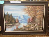 Full view of framed painting depicting mountain, lake, and autumnal trees.