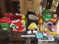 Green M&M cookie jar, two red M&M vases with green M&M figures, and green M&M candy dispenser displayed