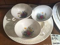 Three handled soup bowls with embossed rim and floral bouquet design on white porcelain.