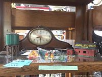 Photo showing the Revere Westminster mantel clock alongside vintage railroad miniatures including a green water tower, Mail Pouch barn, crossing signals, and small figures.
