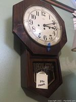 Full view of the wooden regulator wall clock with octagonal shape and glass pendulum window.