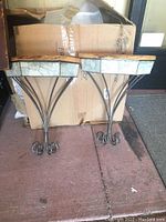 Pair of two handmade wall shelves with natural wood tops, slate inset bands, and wrought iron bases placed on floor with cardboard background.