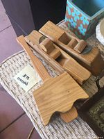 Two wooden hand planes and a wooden mallet placed on a wicker surface. The mallet head is made of light wood with visible wood grain, with a handle of matching wood tone.