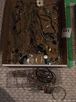 Photo showing assorted bracelets, necklaces, watches, and rings arranged in a box and on the carpet.