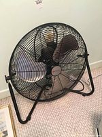 Front view of the large floor fan showing three metallic blades and black protective grille with Utilitech logo on center hub.